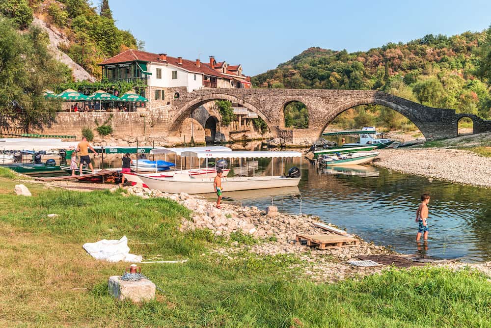 Podgorica, Montenegro - Old arched stone bridge across the river Crnojević. Boat pier and hotel at the source of the river.