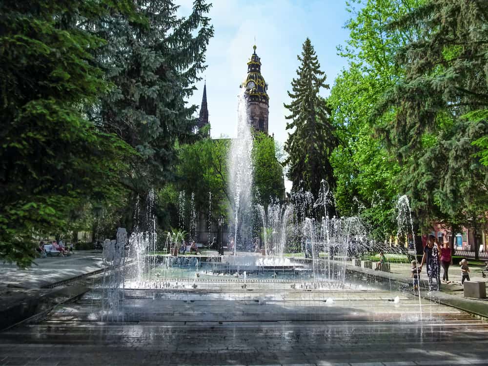Kosice, Slovakia - Jets of water in fountain on background of Cathedral of St. Elizabeth in Kosice Park on a sunny spring day. Cityscape of modern park and tower of ancient Gothic temple
