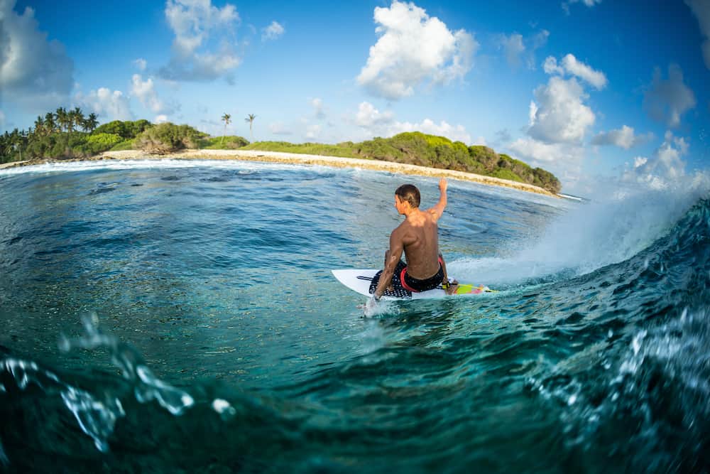 Surfer rides the ocean wave at sunset. Honkeys surf spot in the Maldives