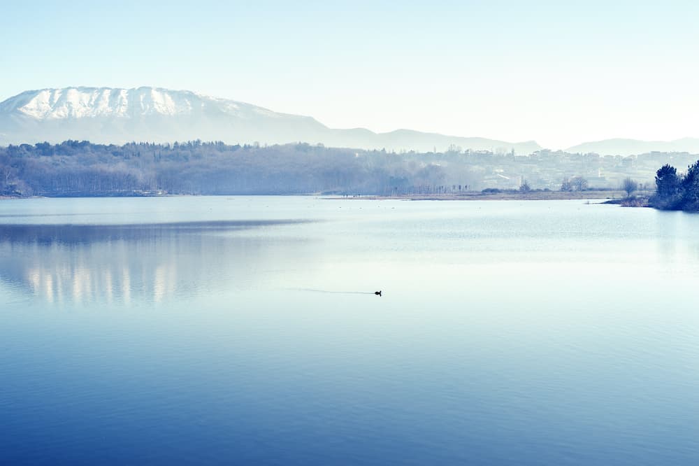 Tirana artificial lake in winter with Dajti mountains with snow and reflection in calm water.