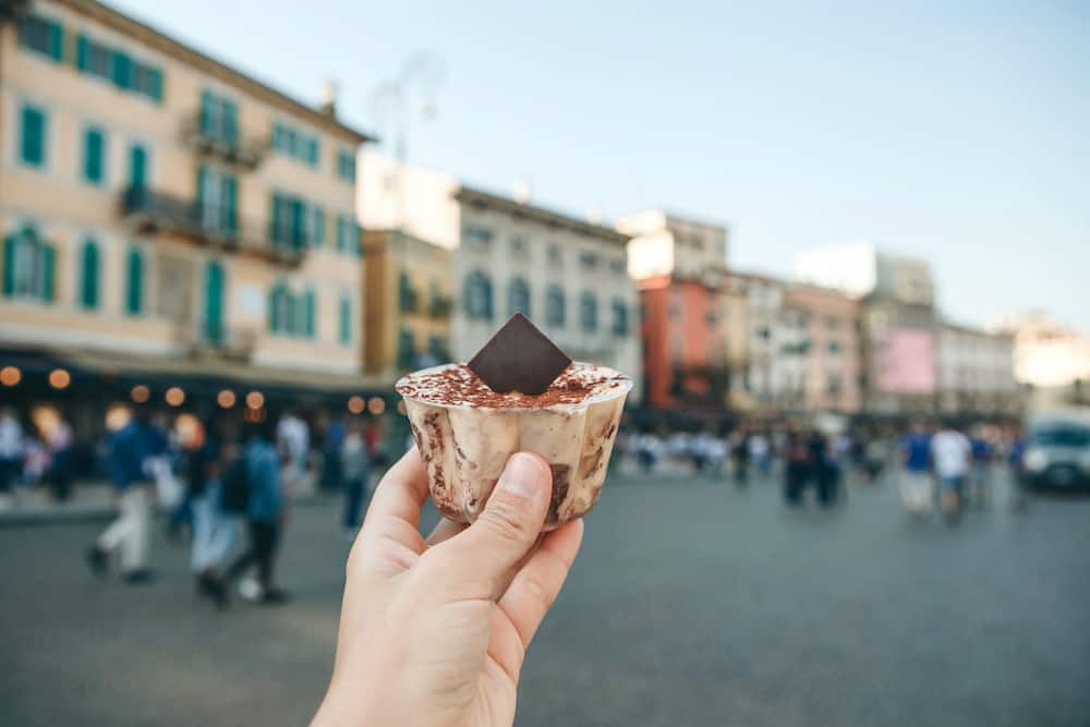 A girl holds in her hand a traditional Italian dessert tiramisu against the background of a street in Verona in Italy.
