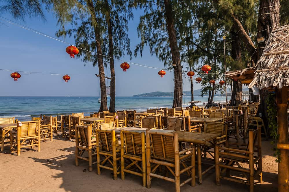 Restaurant on Bang Tao beach Phuket Thailand early in the morning. Bang Tao Bay in the background