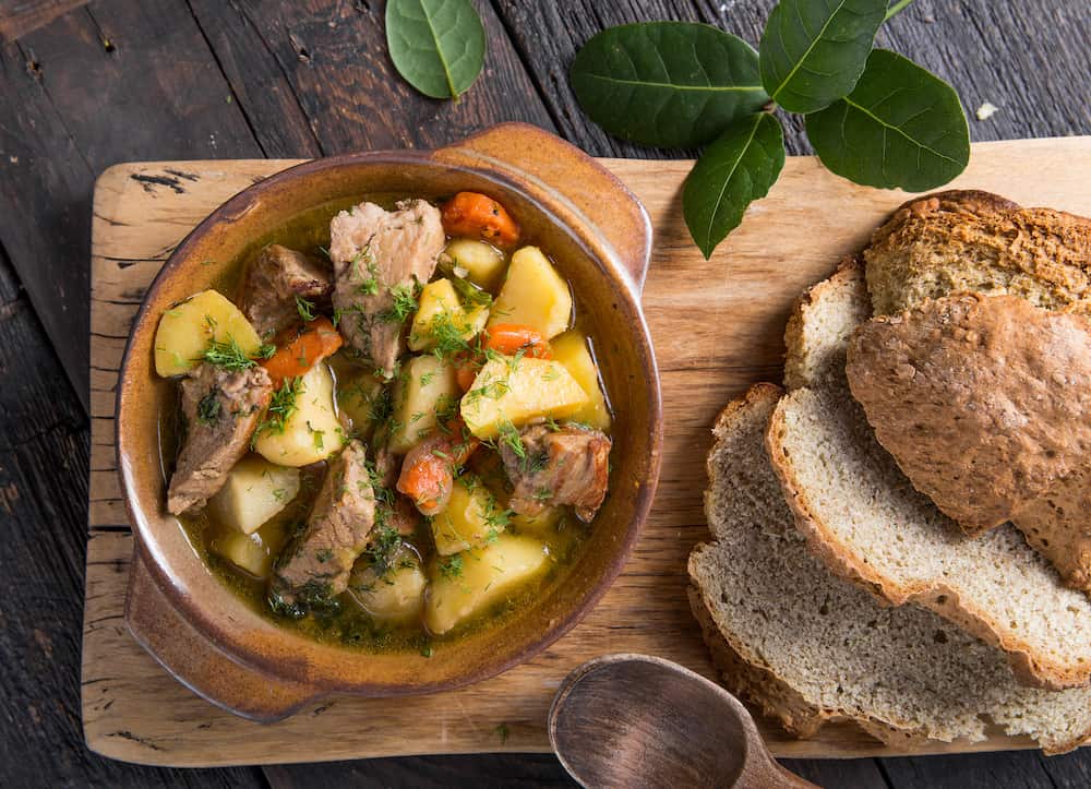 Potato Stew. Irish dinner. Beef meat stewed with potatoes, carrots and soda bread on wooden background, top view, copy space. Homemade winter comfort food - slow cooked
