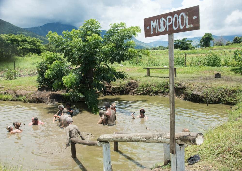NADI, FIJI, PACIFIC ISLANDS- Tourists bathing in mud pool with tropical rainforest landscape under a stormy sky in remote Nadi, Fiji