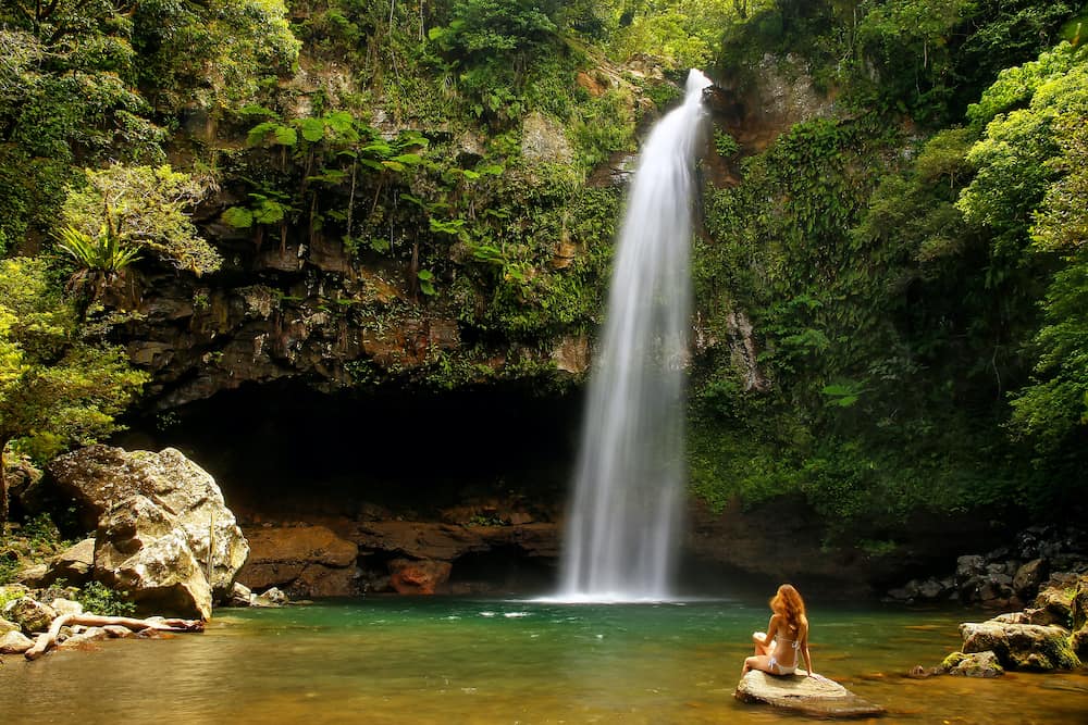 Young woman in bikini sitting by Lower Tavoro Waterfalls in Bouma National Heritage Park on Taveuni Island, Fiji. Taveuni is the third largest island in Fiji.