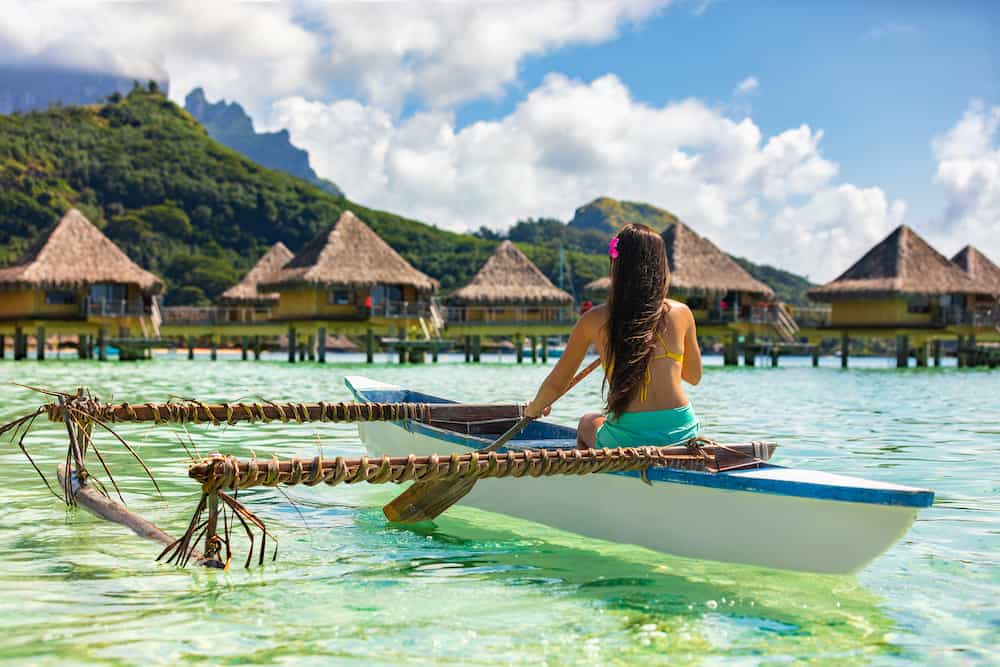 Outrigger Canoe - woman paddling in traditional French Polynesian Outrigger Canoe for recreational activity and watersport competition. Bora Bora with overwater bungalow resort hotel sport lifestyle