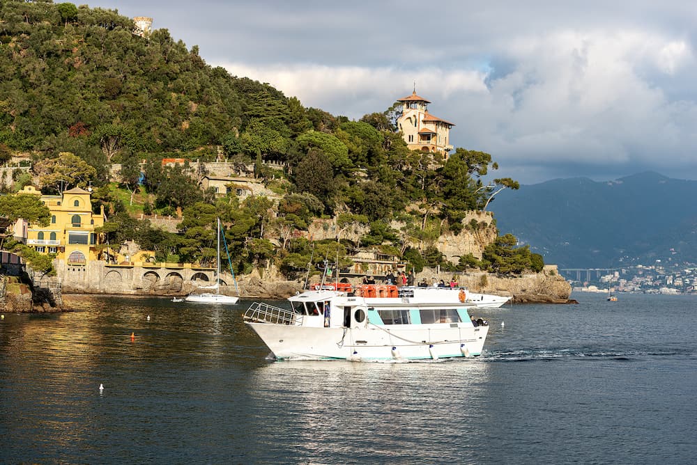 PORTOFINO, LIGURIA, ITALY - : a group of tourists is arriving on a ferry in the port of the famous and ancient village of Portofino, On the hill an ancient villa with tower. Genoa Province, Liguria, Italy, Europe