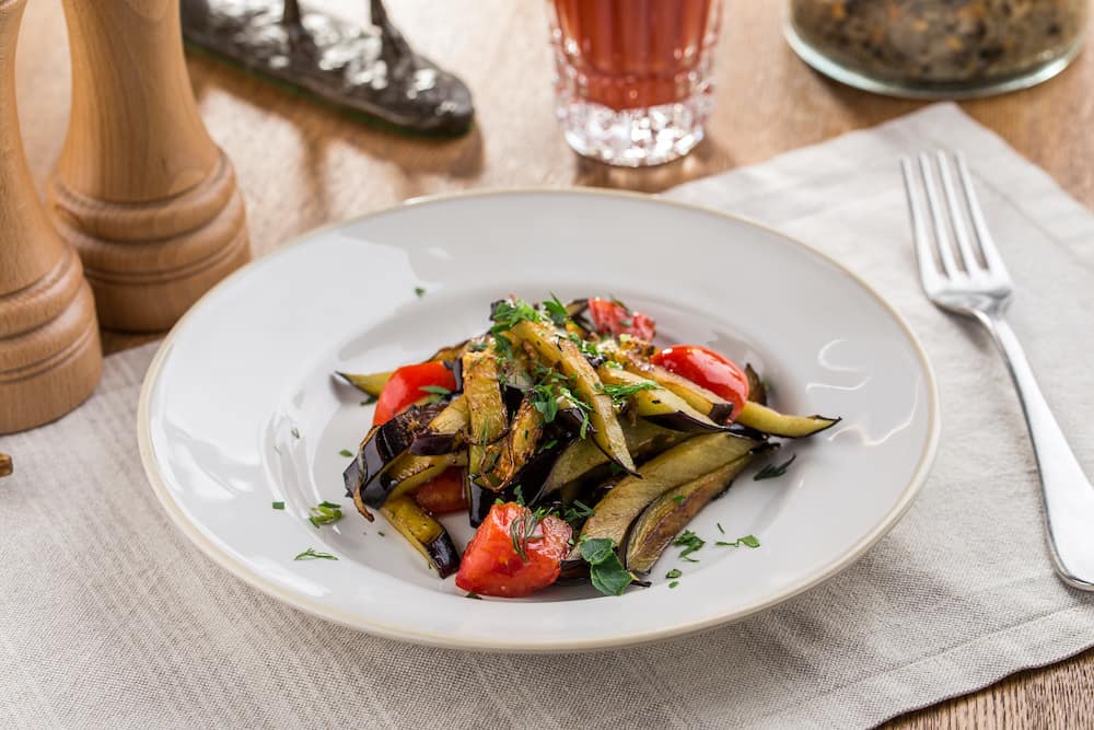 Grilled vegetables warm salad with eggplant and tomato with tomato juice on wooden table side view