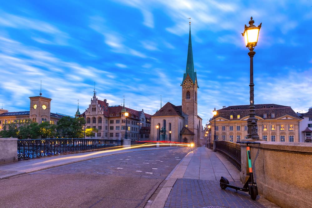 Famous Fraumunster church and Munsterbrucke bridge over river Limmat during evening blue hour in Old Town of Zurich, the largest city in Switzerland