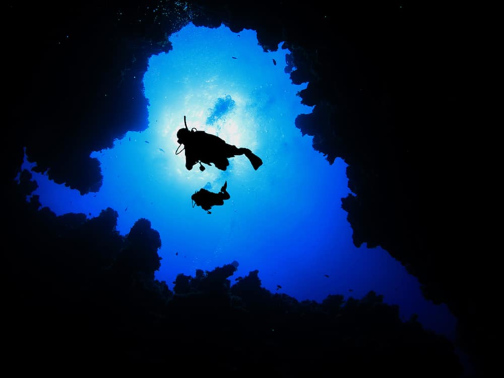 Two Scuba Divers descending into underwater cave