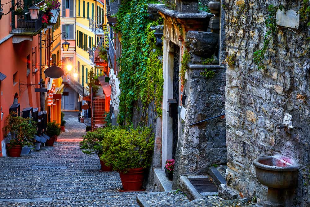 Bellagio, lake Como, Milan, Italy. Famous stone stairs street. Evening Nighttime with blue sky and lights of outdoor lanterns. Picturesque italian architecture of famous luxury Alpine health resort.