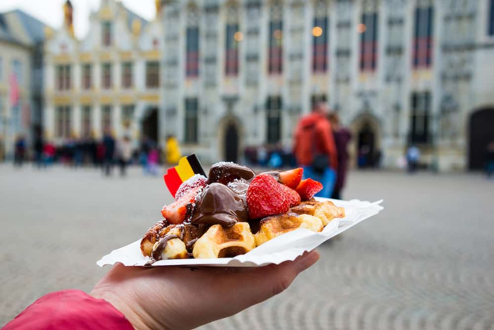 Belgium waffle with chocolate sauce and strawberries, Bruges city background, Belgium.