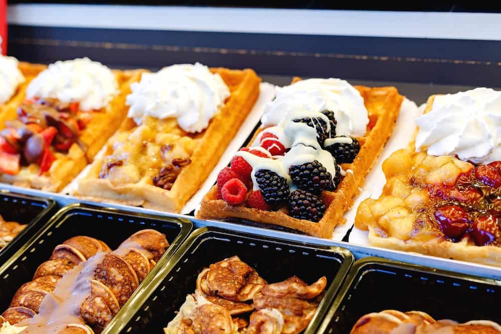 waffles street food with different toppings, fruits, sweets, whipped cream. Showcase pastry shop Belgian waffles of various types. Stock Photo Waffle desserts with berries, cream, chocolate.