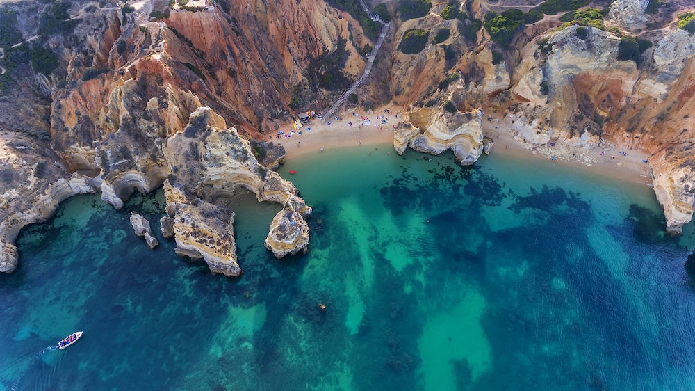 Camilo Beach in Lagos, Algarve - Portugal. Portuguese southern golden coast cliffs. Tourists on the beach. Sunny day aerial view.