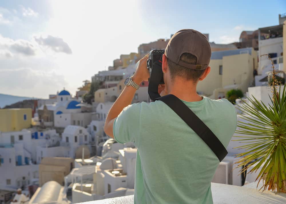 A traveler standing and taking pictures of Oia Town in Santorini, Greece.