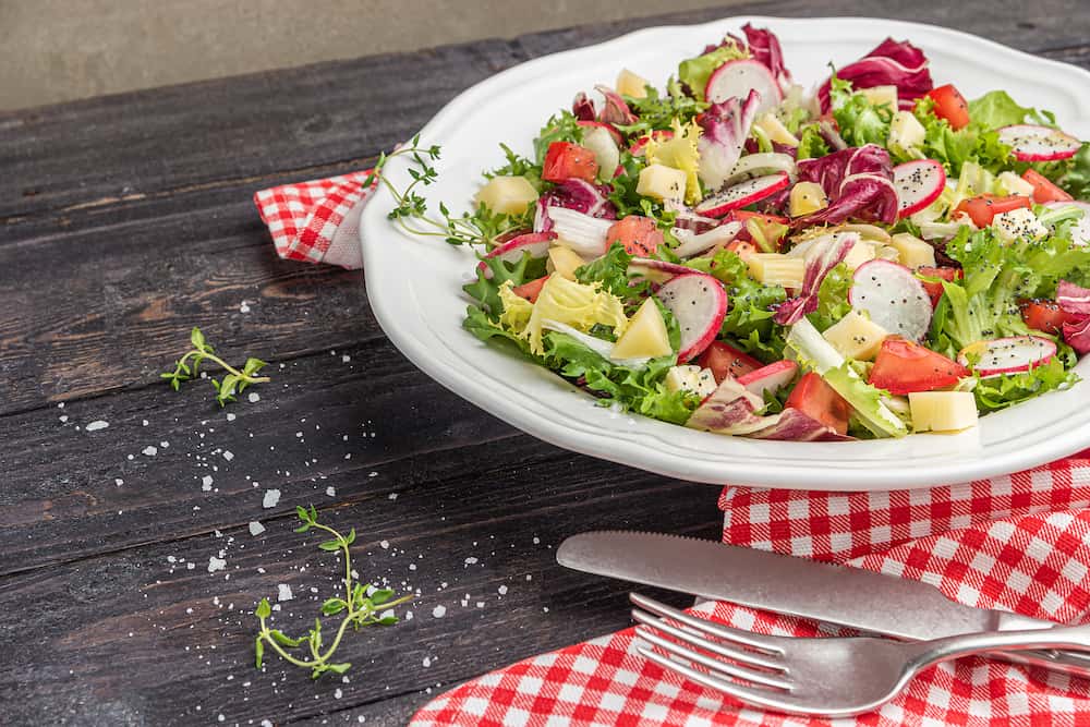 Fresh salad with mixed greens radish cheese and tomato in a plate on wooden background. Italian Mediterranean or Greek cuisine. Vegetarian vegan food. Fresh salad with mixed greens radish cheese and tomato in a plate on wooden background.