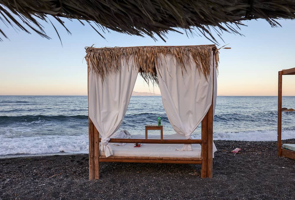 Sun loungers on the black volcanic beach of Kamari in Santorini. Cyclades, Greece