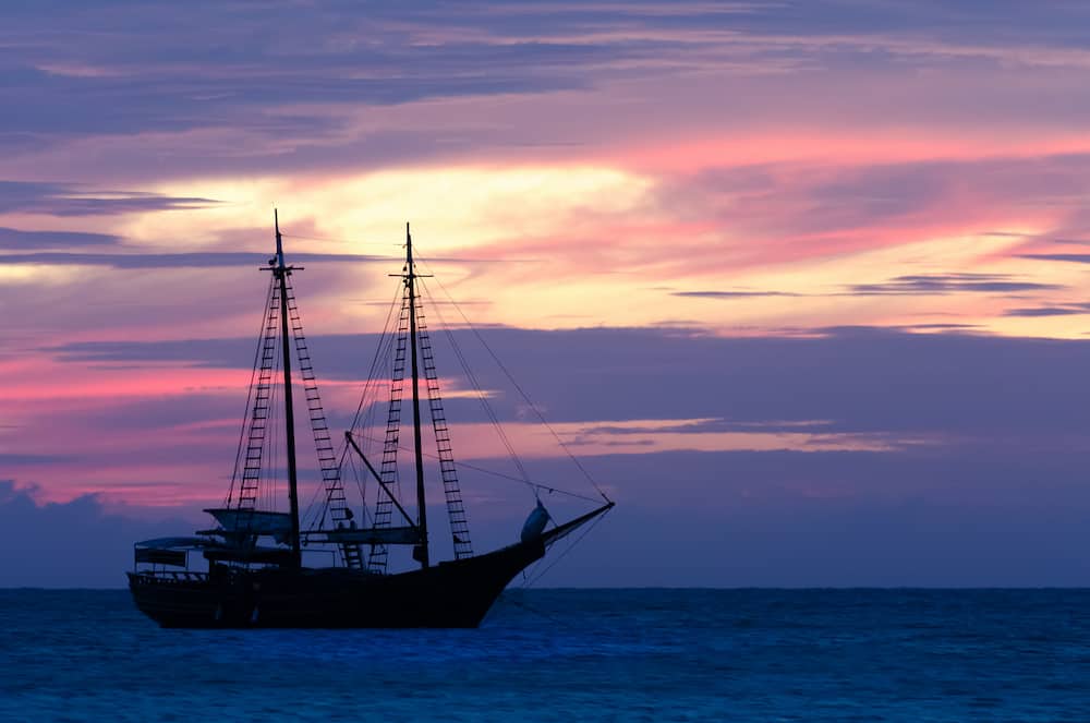 Pirate sailboat on sea navigating towards the sunset. The image was taken from Palm Beach in Aruba in the Caribbean Sea.