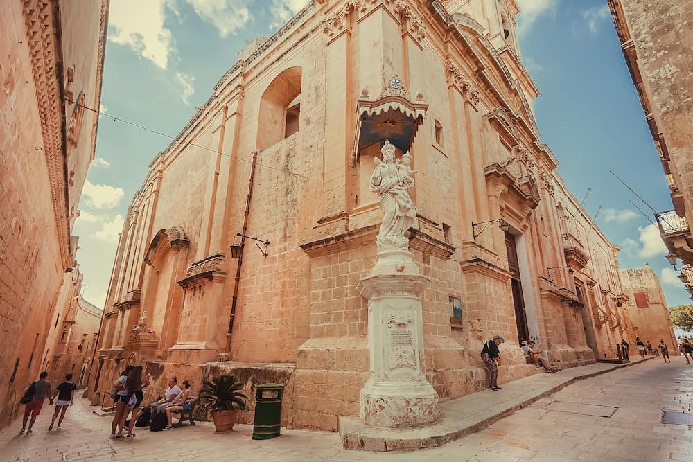 MDINA, MALTA: Corner of narrow streets town with historical brick houses, sculptures and people around. Malta has more than 1.6 million tourists per year