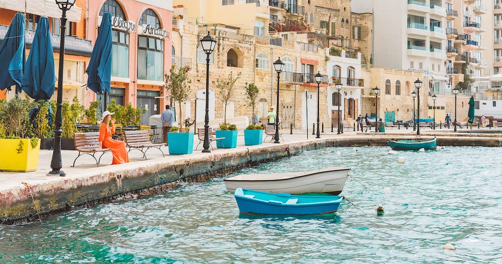 St. Julian. Malta. Beautiful old town of St. Julian on the island of Malta with colourful boats, bay, promenade and a statue of a fisherman with a cat and a fish.