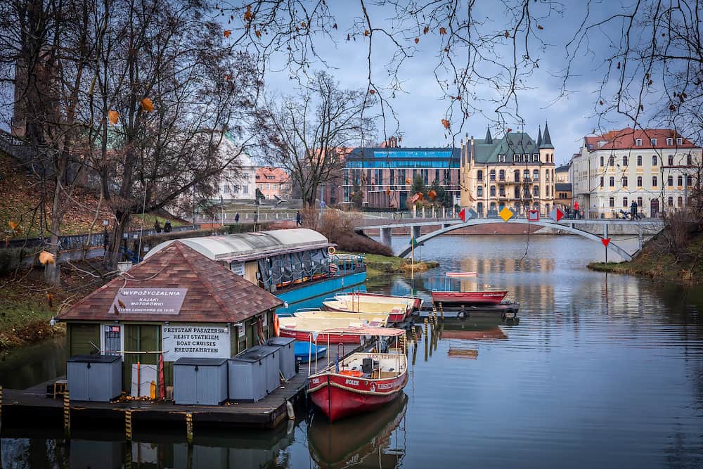 Wroclaw, Poland - Boat rental at Gondola Bay on Odra river on a winter day. Dunikowski boulevard bridge and historical buildings of Ostrow Tumski in background.