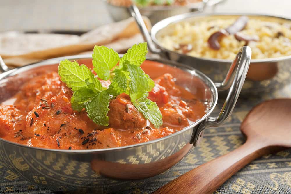 Indian Curry Chicken Tikka Masala - Indian meal of chicken tikka masala, garnished with mint, in a balti dish or karahi, accompanied by pilau rice and chapati.