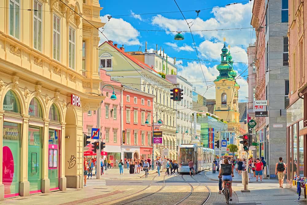Linz - Austria: View through the main street of the city with walking people, shops, tram lines, and a tram