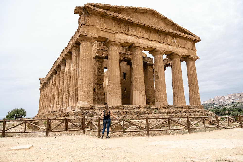 Young beautiful blonde woman amazed at Temple of Concordia, located in the park of the Valley of the Temples in Agrigento, Sicily, Italy