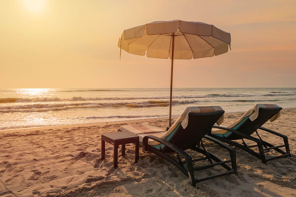 Sun umbrellas and chairs on tropical beach with sunset.