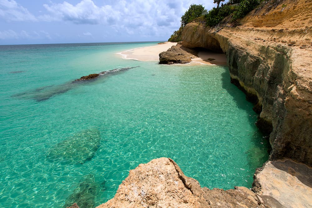 view of rocky rugged shore with white sand beach and turquoise lagoon at anguilla island