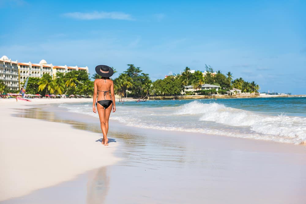 Tourist woman on beach vacation in Barbados island. Caribbean holidays. Dover beach, cruise travel destination. Girl walking with sun hat and bikini relaxing in water.