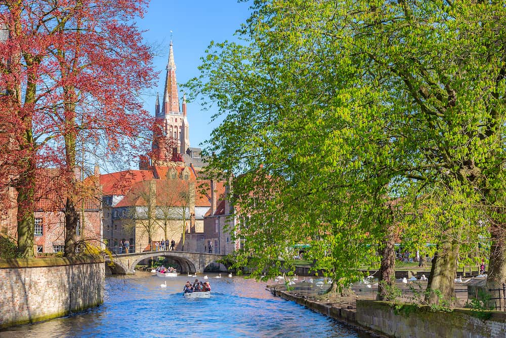 Bruges, Belgium - Spring view with canal and bridge, boat, spring trees and church tower