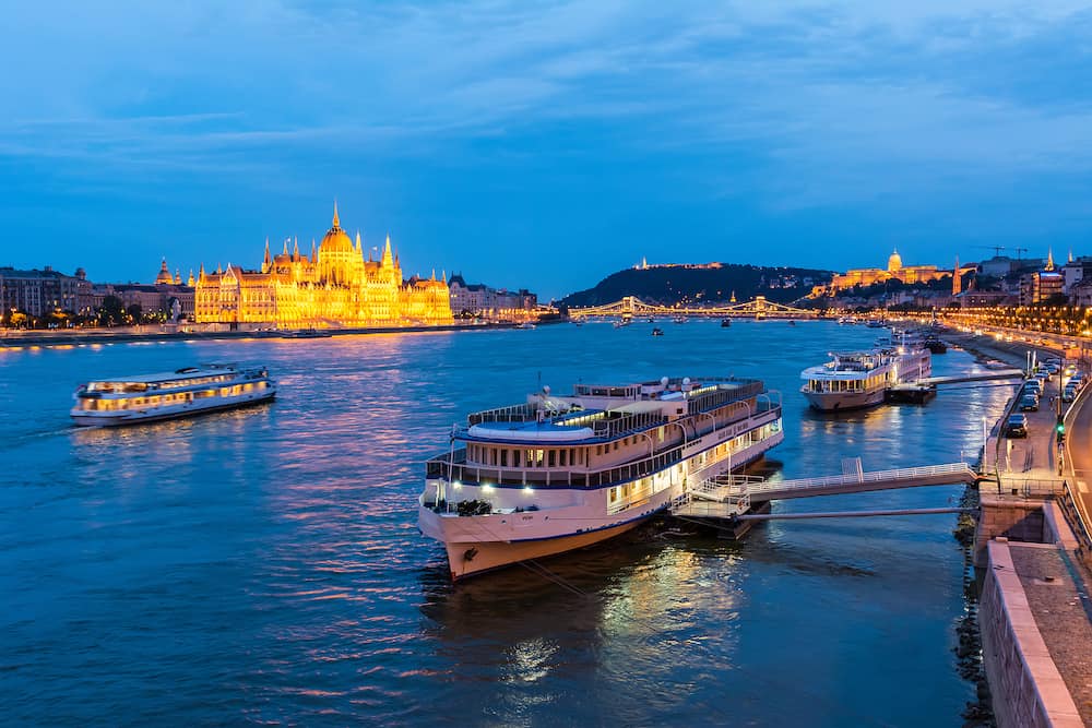 Budapest, Hungary - View of Danube river in Budapest, toward the Parliament building, with cruise boat in the foreground, at night.