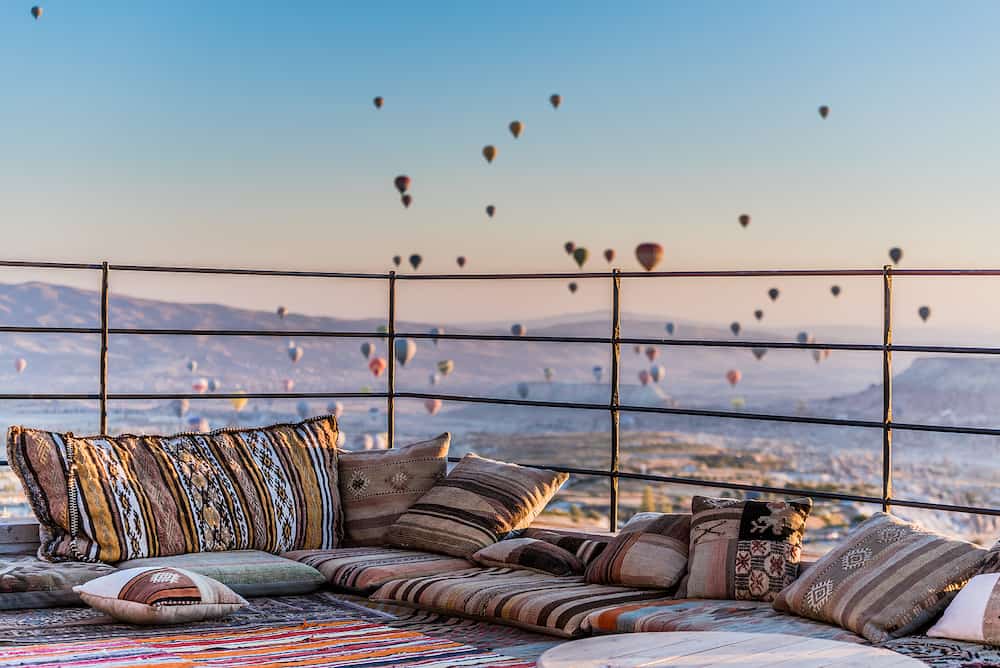Rooftop terrace decorated with pillows and carpets in Turkish style with the view in the morning over balloons in Greme from Uhisar, Cappadocia, Turkey