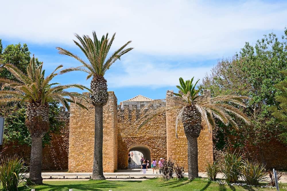 LAGOS, PORTUGAL - View of the entrance arch of the Governors Castle (Castelo dos Governadores) with palm trees in the foreground and tourists enjoying the setting, Lagos, Algarve, Portugal, Europe