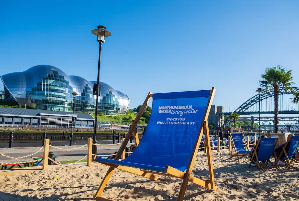 Newcastle, United Kingdom -: Artificial beach setting with sand and beach chairs on a beautiful summer afternoon at Newcastle Quayside with Sage Gateshead and Tyne Bridge in the background.