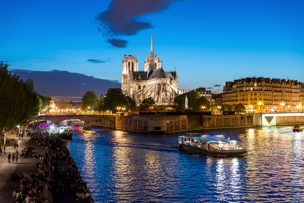 Notre Dame de Paris with cruise ship on Seine river at night in Paris France