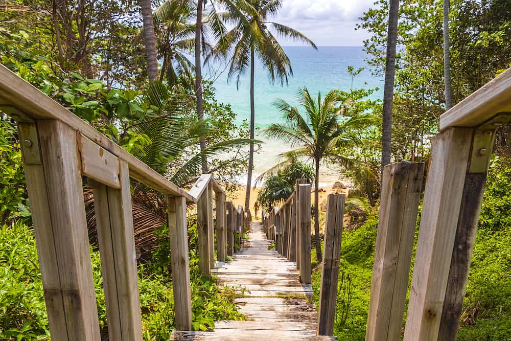 Wood stairs steps down to the Nai Thon Naithon Beach bay and landscape panorama a beautiful dream beach with turquoise clear water and waves in Sakhu Thalang on Phuket island Thailand.