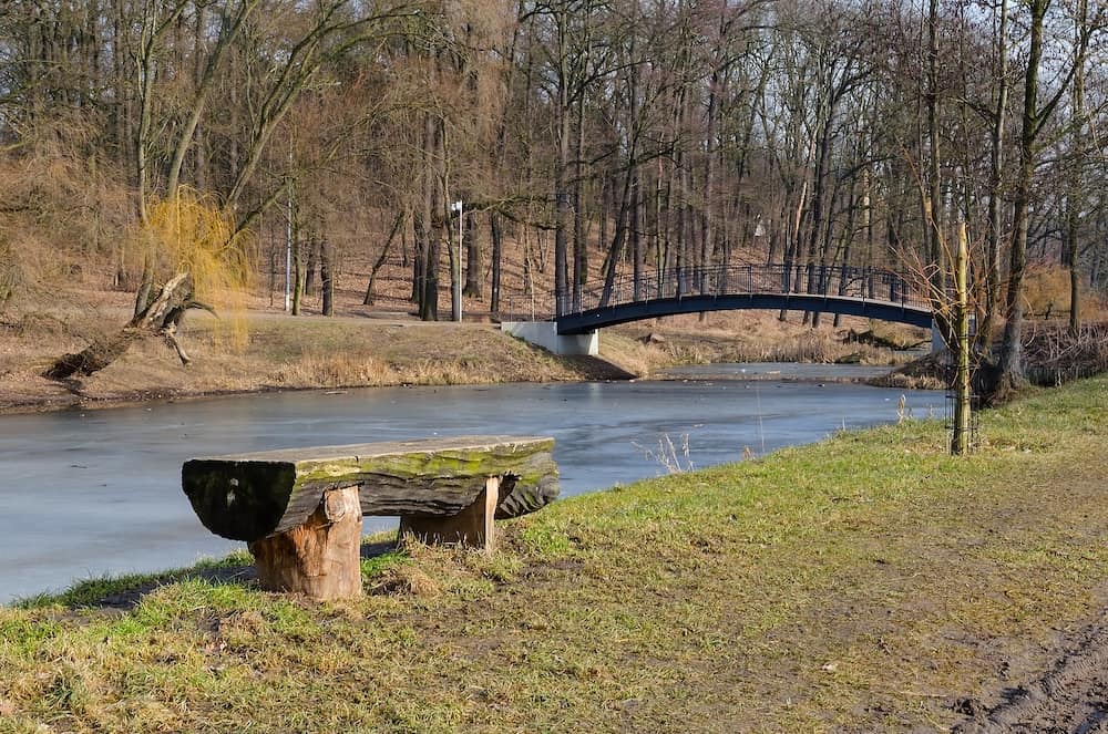 Bench and bridge over the stream sunny day park in Torun, Poland.