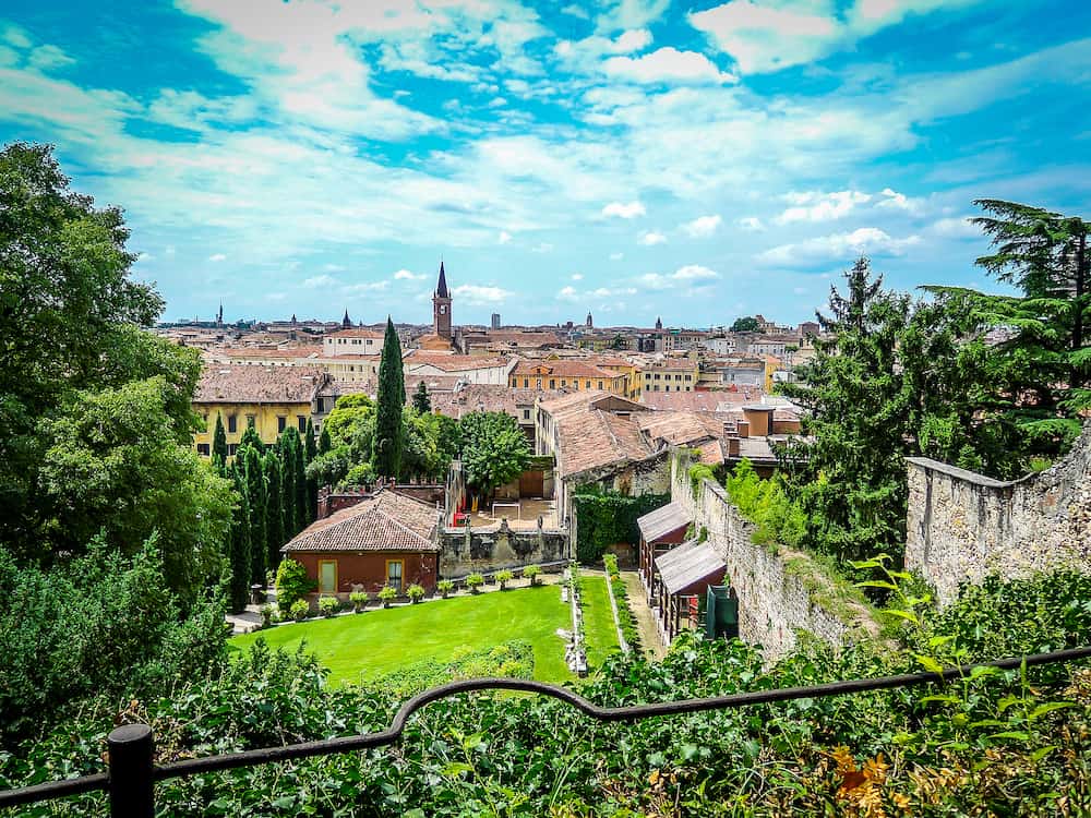 Beautiful view of Giusti gardens and lookout over italian city Verona on bright sunny day. Trees and flowers in front of Verona skyline and houses. No people.