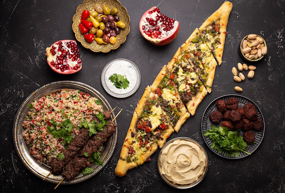 Various Turkish dishes: pide pizza, meat kebab with tabbouleh salad, falafel, hummus, olives, pistachios and Middle Eastern meze on black concrete table top view. Ethnic arab food, cuisine of Turkey