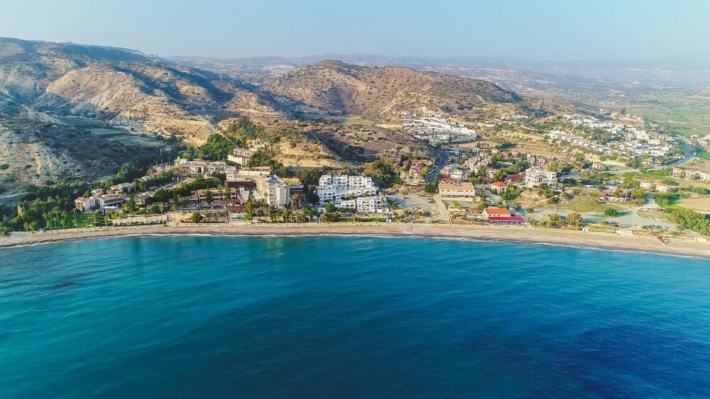 Aerial bird's eye view of Pissouri bay, a village settlement between Limassol and Paphos in Cyprus. Panoramic view of the coast, beach, hotel, resort, hills, plain and building developments from above.