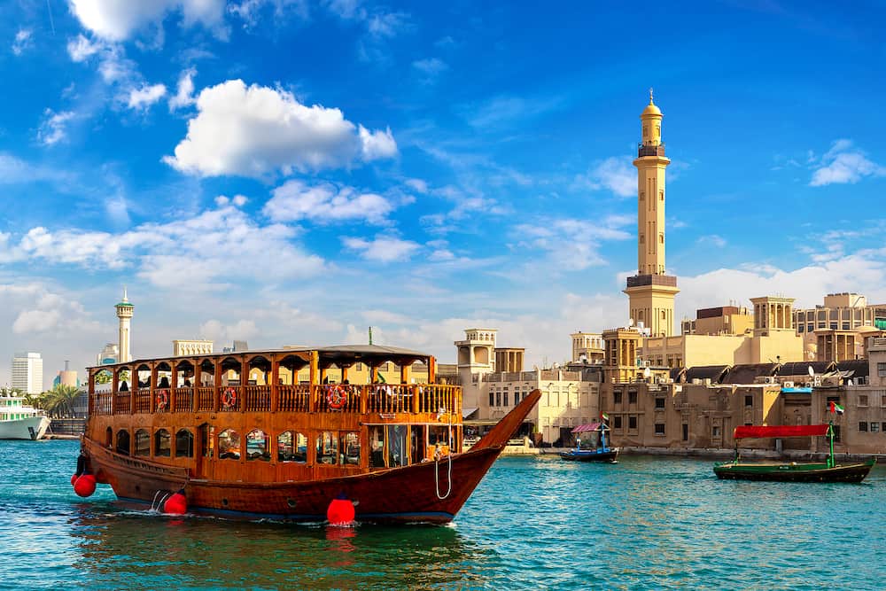 Dhow - old traditional wooden ship and Grand Bur Dubai Masjid Mosque on the bay Creek in Dubai, United Arab Emirates
