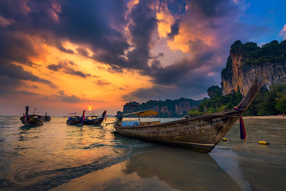 Railay Beach, Thailand - Dramatic sunset over Railay Beach at Krabi, Thailand, with traditional longtail boat in the foreground.