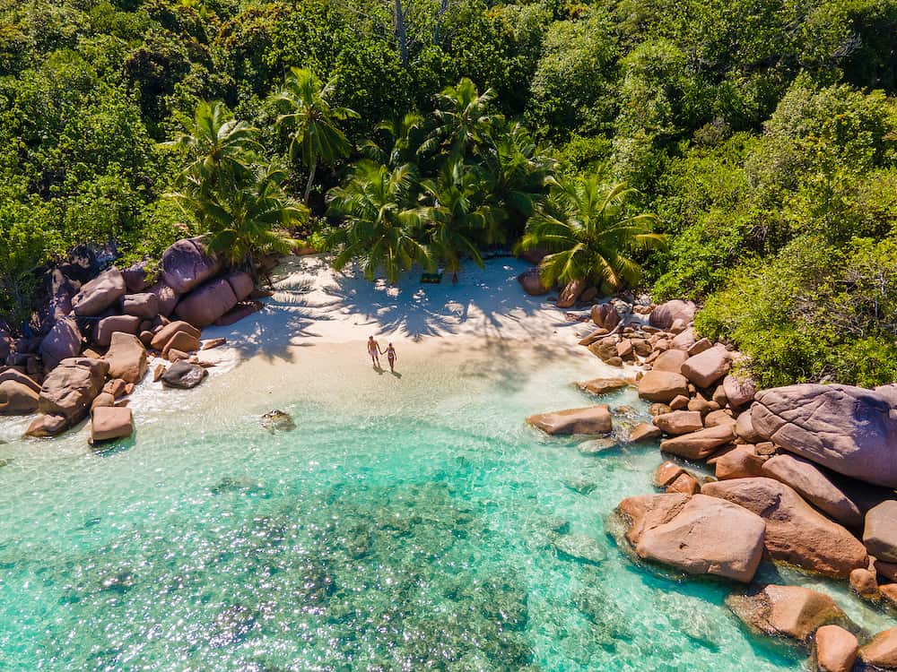 Praslin Seychelles tropical island with withe beaches and palm trees, couple of men and women mid age on vacation at Seychelles visiting the tropical beach Anse Lazio Praslin Seychelles. drone view