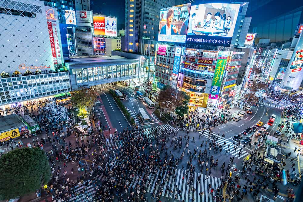 Shibuya, Tokyo, Japan - Top view of crowd people pedestrians walking cross zebra crosswalk in Shibuya district at night in Tokyo, Japan. Lights from commercial billboards.