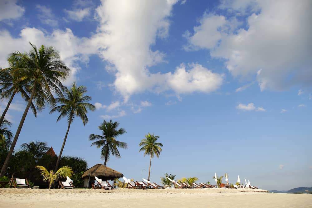 Tourist beach with white sand, palm trees and sun loungers