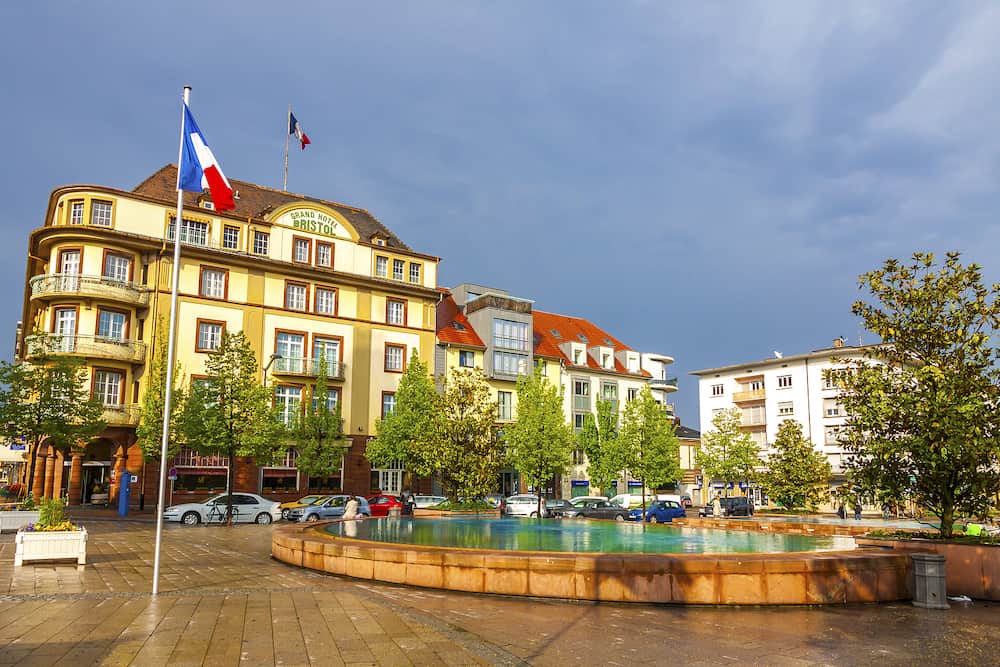Colmar, France - Railway station square (Place de la Gare) in Colmar city, Alcase, France. Square has a beautiful fountain divided into two parts. Grand Hotel Bristoll on background
