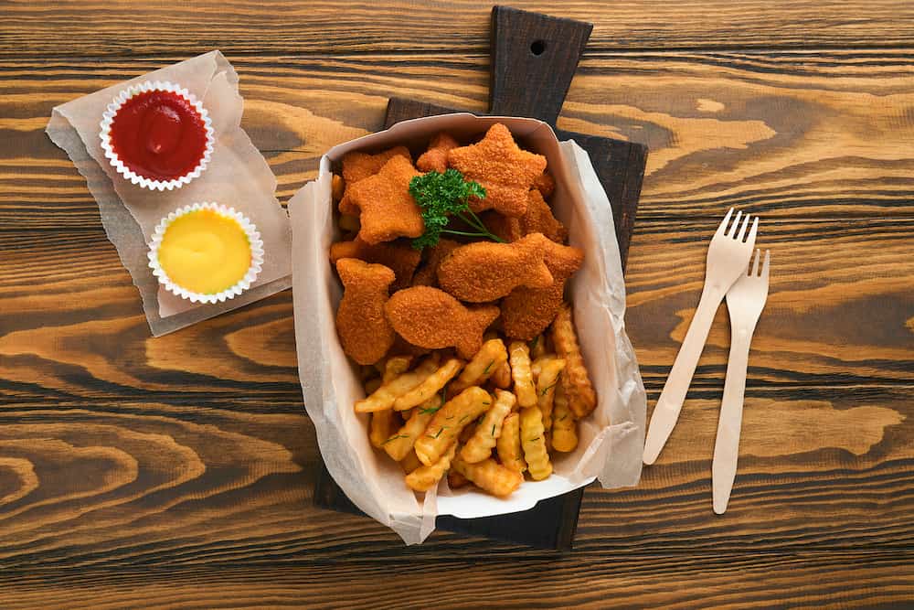 Fish and Chips british fast food. Fish Sticks with french fries set on takeaway paper plate on old wooden table background. Traditional British authentic street food or takeaway food. Mock up.