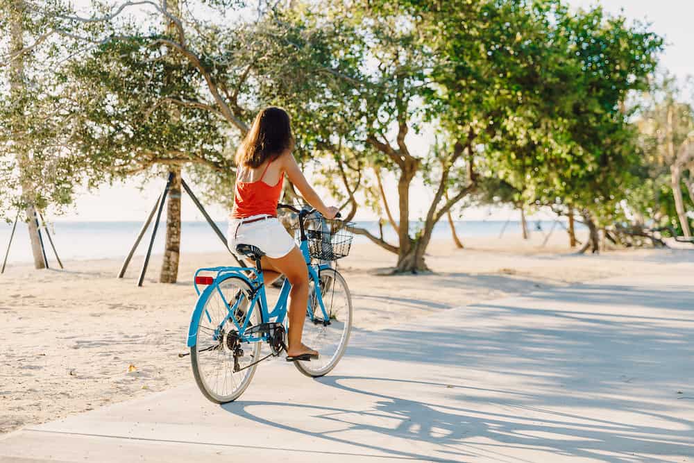 Happy young woman on blue bicycle near ocean in tropical island